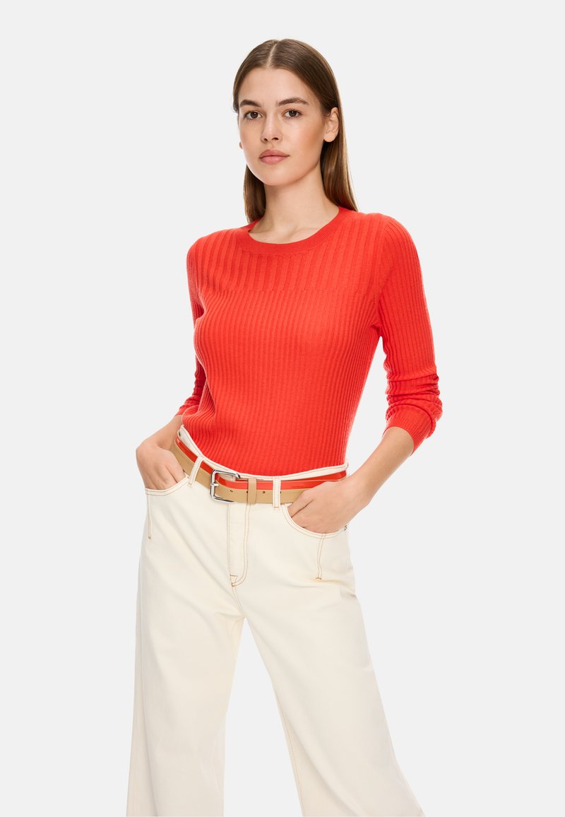 Roter gerippter Pullover mit langen Ärmeln und rundem Halsausschnitt, kombiniert mit creamfarbenen, weit geschnittenen Hosen und einem hellbraunen Gürtel mit silberner Schnalle.