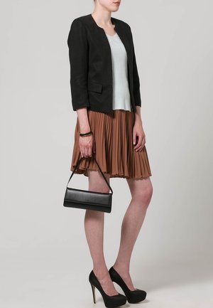 Zwarte blazer, lichtblauw topje, geplooide bruine rok, zwarte hakken en een kleine zwarte handtas. Texturen omvatten lichtgewicht stof en plooien.