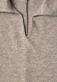 Tissu beige tricoté avec une ouverture de col en V montrant la texture détaillée et les coutures du vêtement.