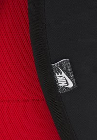 Nike sportkläder i svart och röd färg, med ett strukturerat mesh-mönster på det röda området och en liten Nike-etikett sydd på.