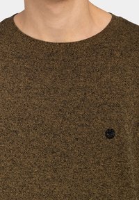 Ciemnobrązowy dziany sweter z okrągłym dekoltem, prążkowanym kołnierzem i małym czarnym logo na piersi. Miękka faktura z delikatnym wzorem.