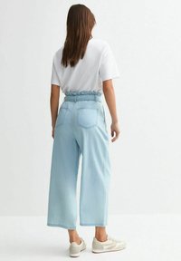 Ljust blå vida jeans med hög midja och samlad elastisk midja; bakfickor synliga, bärs med en vit t-shirt och neutrala sneakers.
