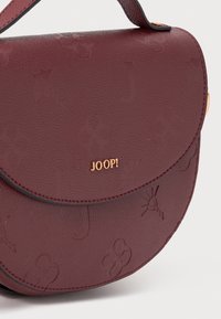 Borsa a tracolla in finta pelle color borgogna con motivi floreali in rilievo, forma rotonda, hardware dorato e dettagli a contrasto in nero.