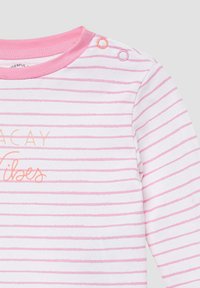 Langärmliges Babyshirt mit weißen und rosa Streifen, pinkem Kragen, zwei Druckknöpfen an den Schultern und dem Text "Urlaubsstimmung" in pastellorange und rosa Buchstaben.