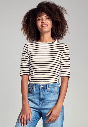 Stribet, kortærmet bluse i creme med sorte striber, lavet af letvægtsstof. Parret med lyseblå højmidjejeans.