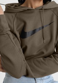 Olivgrön hoodie med en svart Nike swoosh-logga. Har en huva med dragsko och raglanärmar, tillverkad av mjukt, strukturerat tyg.