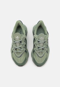 Zelené sportovní boty s texturovaným textilním svrškem, síťovinovými akcenty a reflexními tkaničkami, s robustní podrážkou a logem Adidas na jazyku.