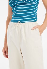 Lichtbeige katoenen broek met een elastische tailleband, een trekkoord en zijzakken. Gecombineerd met een mouwloos top met blauwe en witte strepen.
