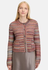 Woman with straight blonde hair wearing a multicolored knit cardigan with buttons over a taupe satin skirt.
