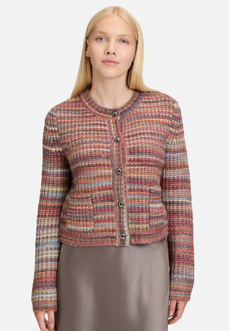 Woman with straight blonde hair wearing a multicolored knit cardigan with buttons over a taupe satin skirt.