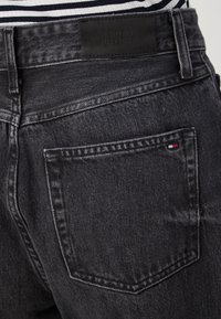 Black denim jeans with a classic cut, featuring a leather patch labeled "TOMMY HILFIGER" and a small logo on the back pocket.