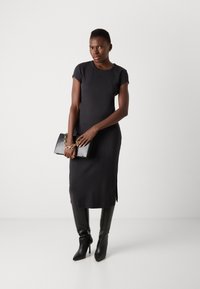 Black, fitted dress with short sleeves, side slits, and a round neckline. Paired with black high boots and a black clutch featuring a chain.