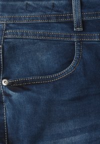 Jeans de mezclilla azul oscuro con un bolsillo frontal con un botón de metal. Textura suave con costuras visibles y un ligero desvanecimiento.