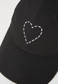 Schwarze Baseballmütze aus strukturiertem Stoff mit einem weiß gestickten Herzmotiv auf der Vorderseite. Gebogener Schirm mit Nähdetails.