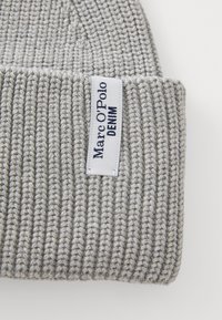 Svijetlosiva rebrasta pletena kapa s bijelom oznakom ušivenom na rubu koja kaže "Marc O'Polo DENIM" u mornarskom plavetnilu.