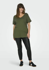 Olijfgroene korte mouw V-hals t-shirt gecombineerd met zwarte slim-fit broek en zwarte sneakers. Zachte textuur, casual ontwerp, relaxte pasvorm.