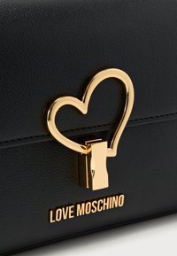 Μαύρη τσάντα χειρός από ψεύτικο δέρμα με χρυσό κλείστρο σε σχήμα καρδιάς και το λογότυπο "LOVE MOSCHINO" σε χρυσά γράμματα. Υφή με ανάγλυφη επιφάνεια, καλοσχηματισμένο σχέδιο.