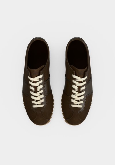 Paire de chaussures décontractées en cuir marron foncé avec des lacets blancs, vue de dessus sur un fond neutre.