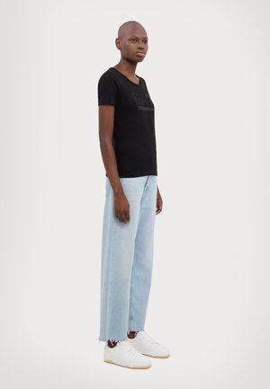 T-shirt noir ajusté avec un col rond, associé à un jean large bleu clair et des baskets blanches à semelle en gomme.