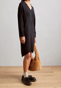 Abito in maglia nero con scollo a V, maniche lunghe e spacchi laterali. Una borsa marrone pelosa e scarpe nere con nappe completano l'outfit.