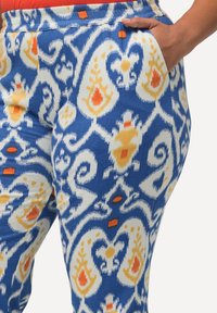 Pantalons bleus à motifs présentant un design complexe avec des accents orange et jaune. Fabriqués en tissu doux, avec des poches latérales pour plus de praticité.