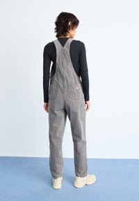 Gray cotton overalls with a relaxed fit, adjustable straps, and front and back pockets, paired with light-colored shoes.