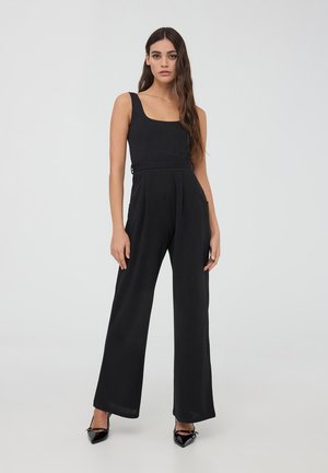 Tuta nera con un corpino aderente e pantaloni a gamba larga. Presenta uno scollo quadrato, tasche laterali e una texture di tessuto liscia.