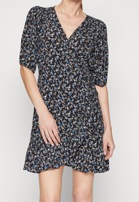 Robe fleurie avec un fond noir, ornée de fleurs blanches et bleues, à manches courtes bouffantes, décolleté en V et ourlet à volants. Tissu léger.