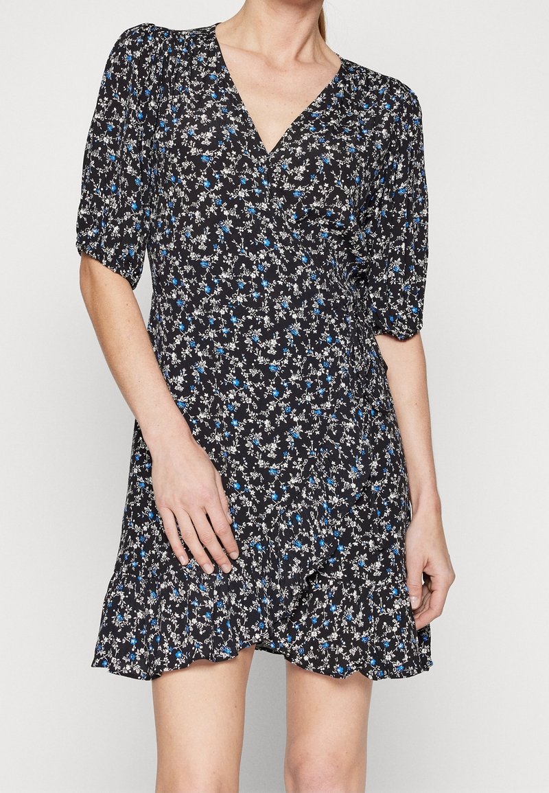 Robe fleurie avec un fond noir, ornée de fleurs blanches et bleues, à manches courtes bouffantes, décolleté en V et ourlet à volants. Tissu léger.