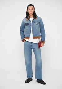 Denim jacket with brown faux leather collar, two chest pockets, button closure, worn with a white T-shirt and light blue wide-leg jeans.