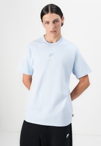 Gaiši zils kokvilnas T-krekls ar apaļu kaklu, īsām piedurknēm un nelielu, tumši zilu Nike logo izšuvumu uz krūšu daļas.