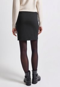 Czarna mini spódniczka o gładkiej fakturze, z bocznymi guzikami. Połączona z nieprzejrzystymi czarnymi rajstopami i czarnymi botkami za kostkę.