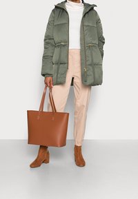 Grön puffjacka med huva, dragkedjestängning och elastisk midja; brun läderhandväska; beigefärgade tapered byxor; bruna ankelstövlar.