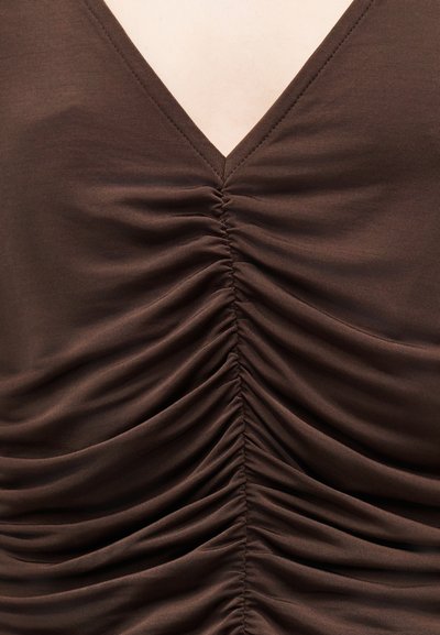 Καφέ ύφασμα με λαιμόκοψη σε σχήμα V και ρυτιδώσεις που διατρέχουν κάθετα το κέντρο.