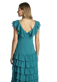 Abito teal con maniche a volant e scollatura profonda a V sul retro. Presenta volant a strati lungo l'orlo e una zip nascosta sul retro.