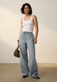 Débardeur blanc côtelé associé à un jean bleu clair à jambes larges avec une taille élastique et des poches latérales, tenu avec un sac à main marron.