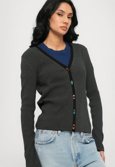 Gray ribbed cardigan with a black trim, featuring colorful decorative buttons. The design has a V-neck and long sleeves. Paired with a blue shirt.