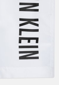 Tessuto bianco con una superficie liscia, caratterizzato da grandi lettere nere che spellano "KLEIN" verticalmente lungo il lato. Nessun hardware o accentuazione visibile.