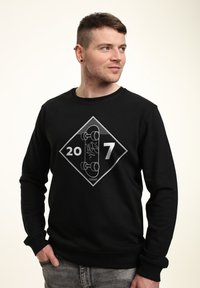 Felpa nera con grafica a forma di diamante che presenta i numeri "20" e "7", insieme a un'illustrazione di skateboard in bianco.