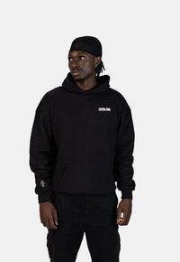 Czarna bluza z kapturem wykonana z bawełny, z kieszenią z przodu, z białym logo "CRYSTAL PARIS" na piersi oraz dekoracyjną grafiką na rękawie.