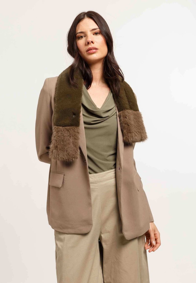 Olivengrønt tørklæde med bløde imiterede pelsender, lagdelt over en beige blazer, komplementeret af en draperet olivengrøn top og beige bukser.