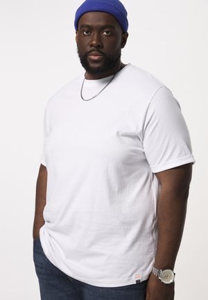 Witte katoenen t-shirt met opgerolde korte mouwen, ronde halslijn en een klein label aan de onderrand. Draag dit met blauwe spijkerbroeken en een blauwe beanie.