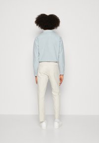 Camicia azzurra chiara con colletto e maniche lunghe abbinata a pantaloni a gamba affusolata di colore crema e sneakers bianche, vista da dietro. Texture morbide.
