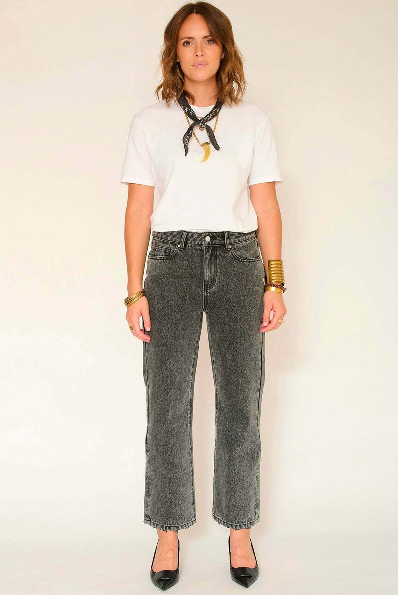 Jean en denim noir et gris à jambes larges avec un ourlet effiloché et une taille haute, porté avec un t-shirt blanc et un foulard noir noué autour du cou.