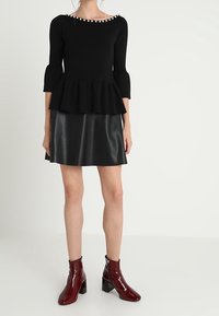 Czarna dzianinowa bluzka peplum z perłowymi akcentami przy dekolcie, połączona z czarną skórzaną mini spódnicą i burgundowymi lakirowanymi botkami za kostkę.