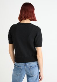 Zwarte gebreide trui met korte mouwen en een geribbelde zoom en ronde hals, gedragen met blauwe high-waisted jeans. Minimalistisch ontwerp.