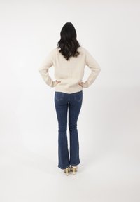 Dikke romige gebreide trui met ribbelzoom, gecombineerd met blauwe uitlopende jeans. De outfit heeft een ontspannen pasvorm en een gestructureerd breipatron.