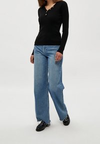 Svart ribbat långärmat topp med knappdetaljer, kombinerat med högmidjade ljusblå vida jeans med fransade nederkanter.