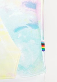 Tissu tie-dye pastel avec des nuances douces de bleu, rose et jaune, comportant une petite étiquette avec un drapeau arc-en-ciel de la fierté sur le bord droit.