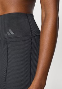 Μαύροι ριμπ κολάν με ψηλή μέση, με τονικό λογότυπο Adidas και υφασμάτινη υφή. Περιλαμβάνει ορατές λεπτομέρειες ραφής.